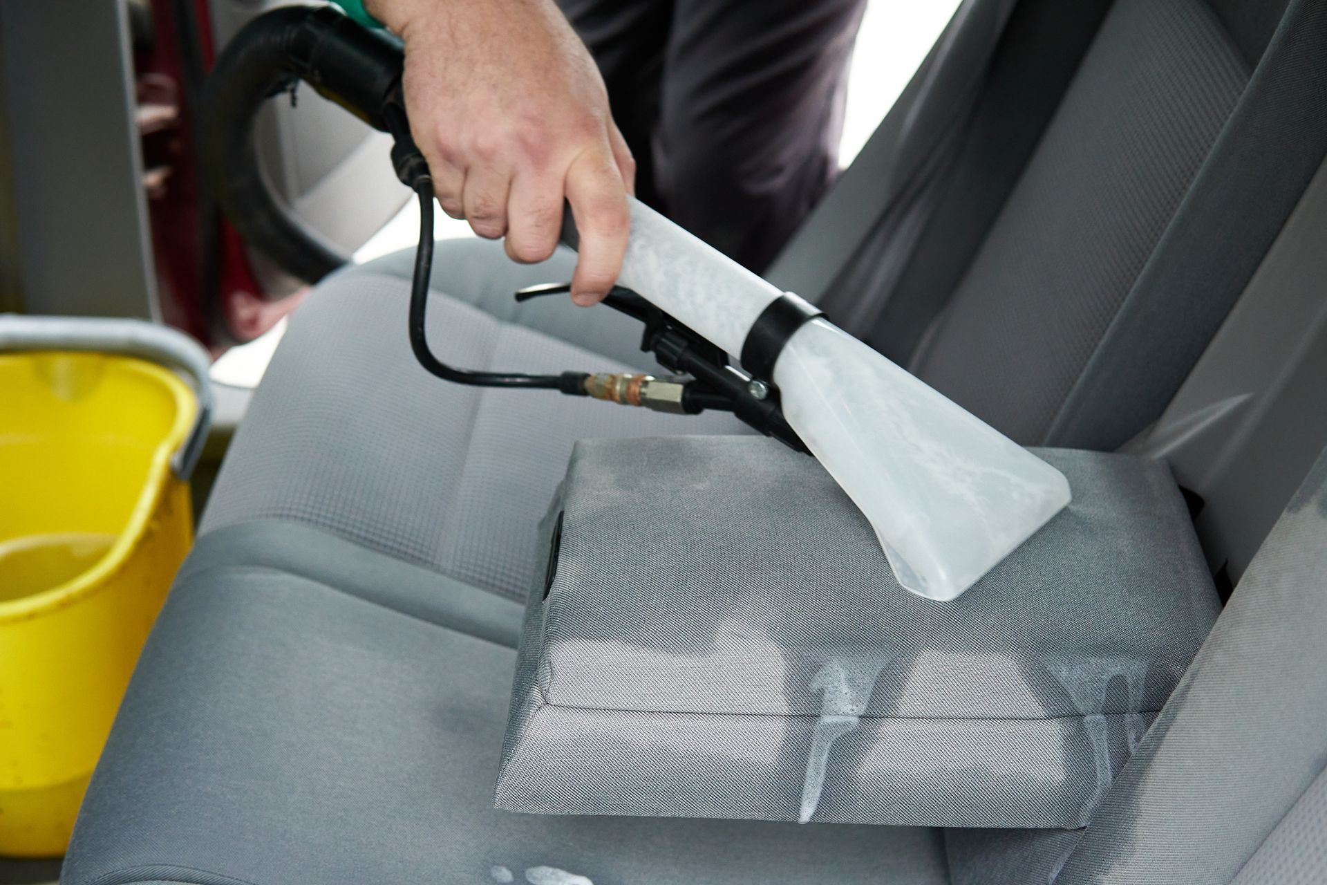 A person cleaning a car seat with a handheld upholstery cleaning tool.