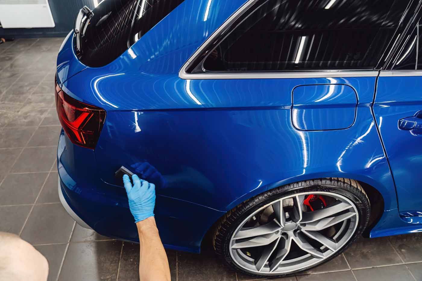 A person in blue gloves polishing a bright blue car.