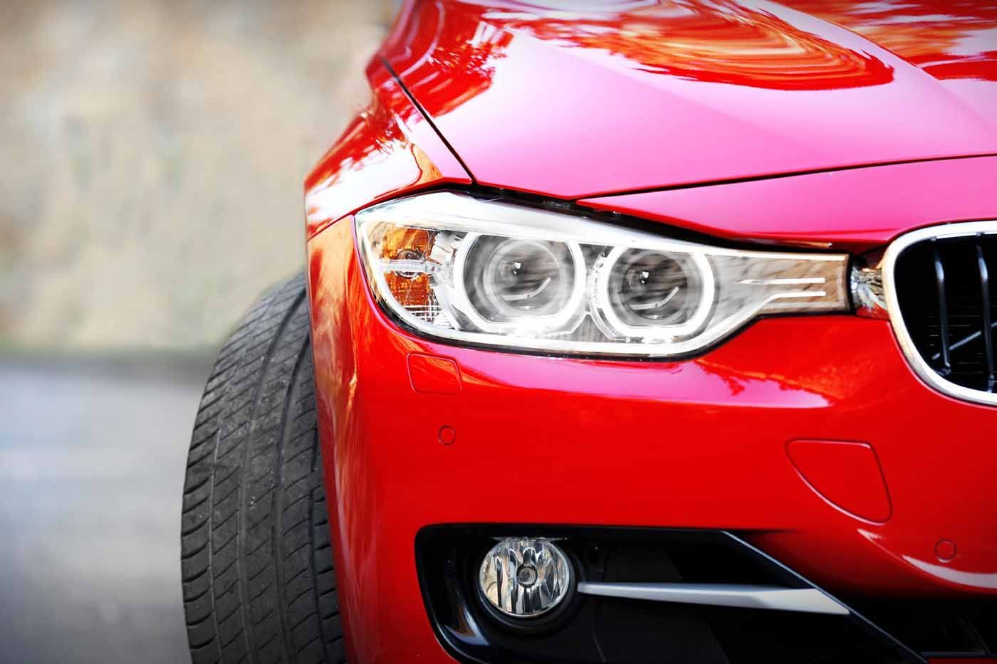 Red car, close-up of the front, highlighting headlight and tire.