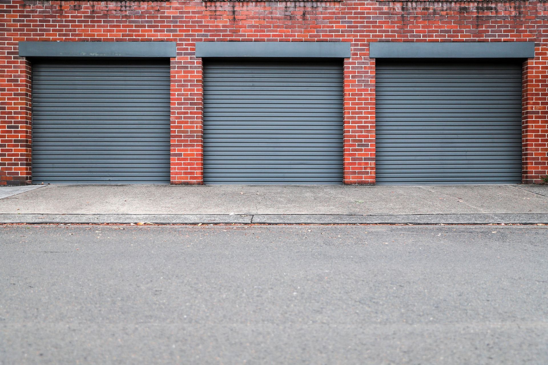Three garage doors are closed on a brick building.