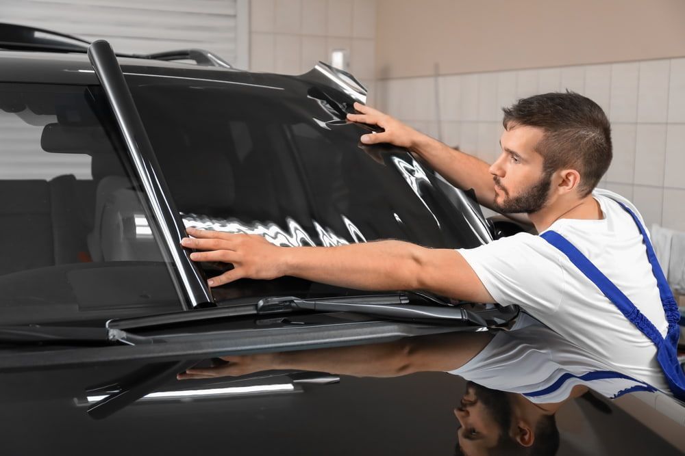 A Man Is Applying Tinted Glass to A Car Window — A1 Windscreens in Tamworth, NSW