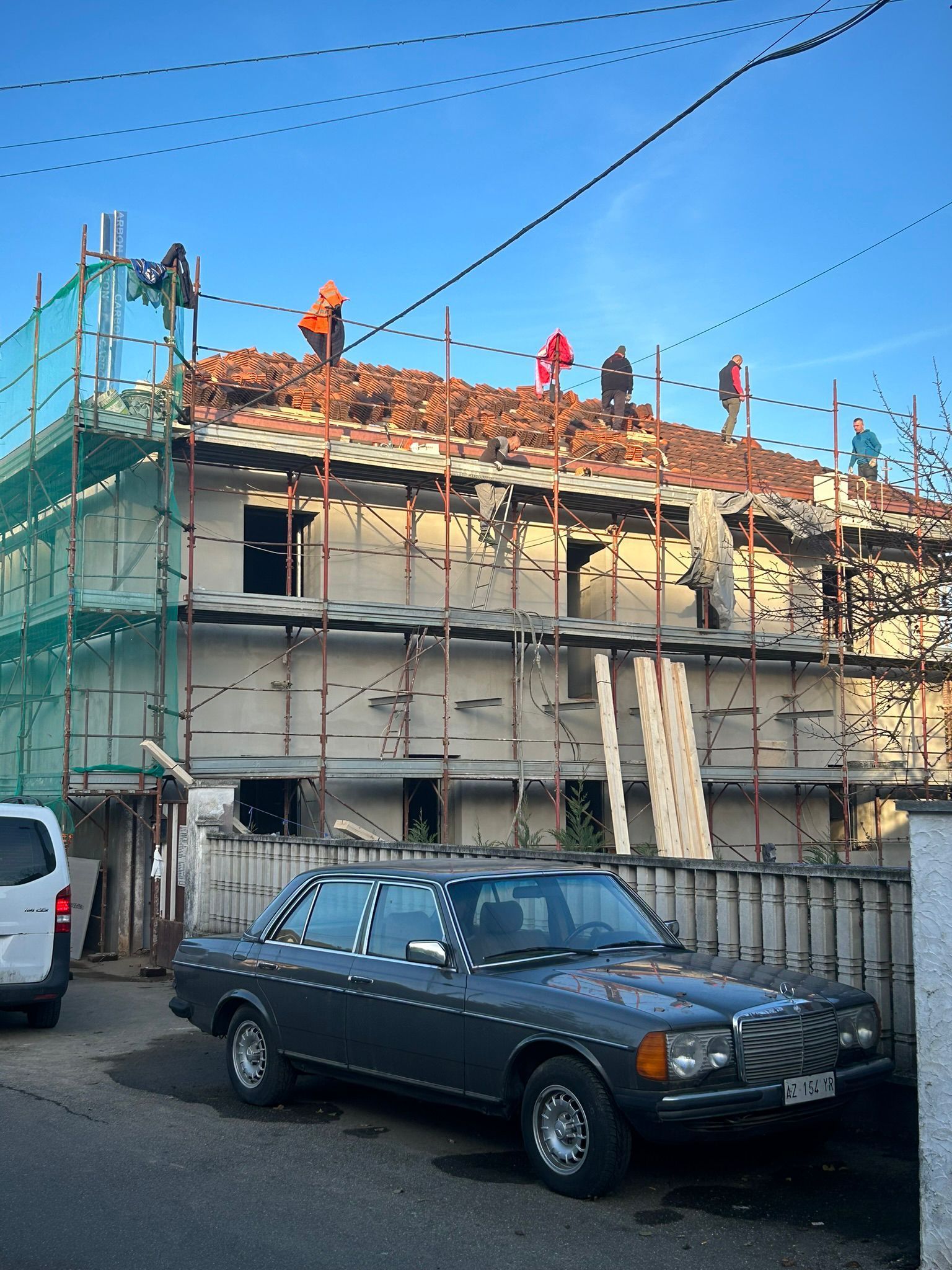 Operai edili sul tetto di un edificio, circondati da impalcature. Un'auto è parcheggiata sulla strada sottostante.