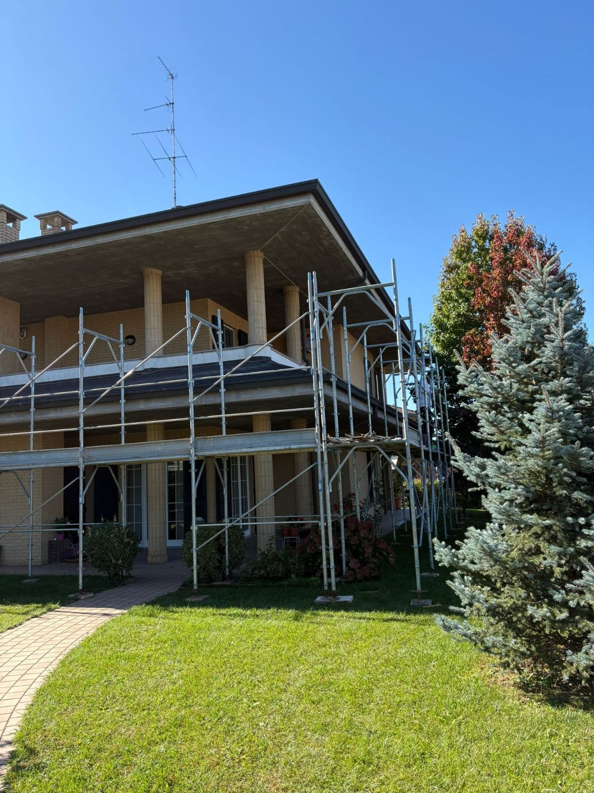 Una casa con impalcature pronte per la ristrutturazione, circondata da erba verde e alberi.