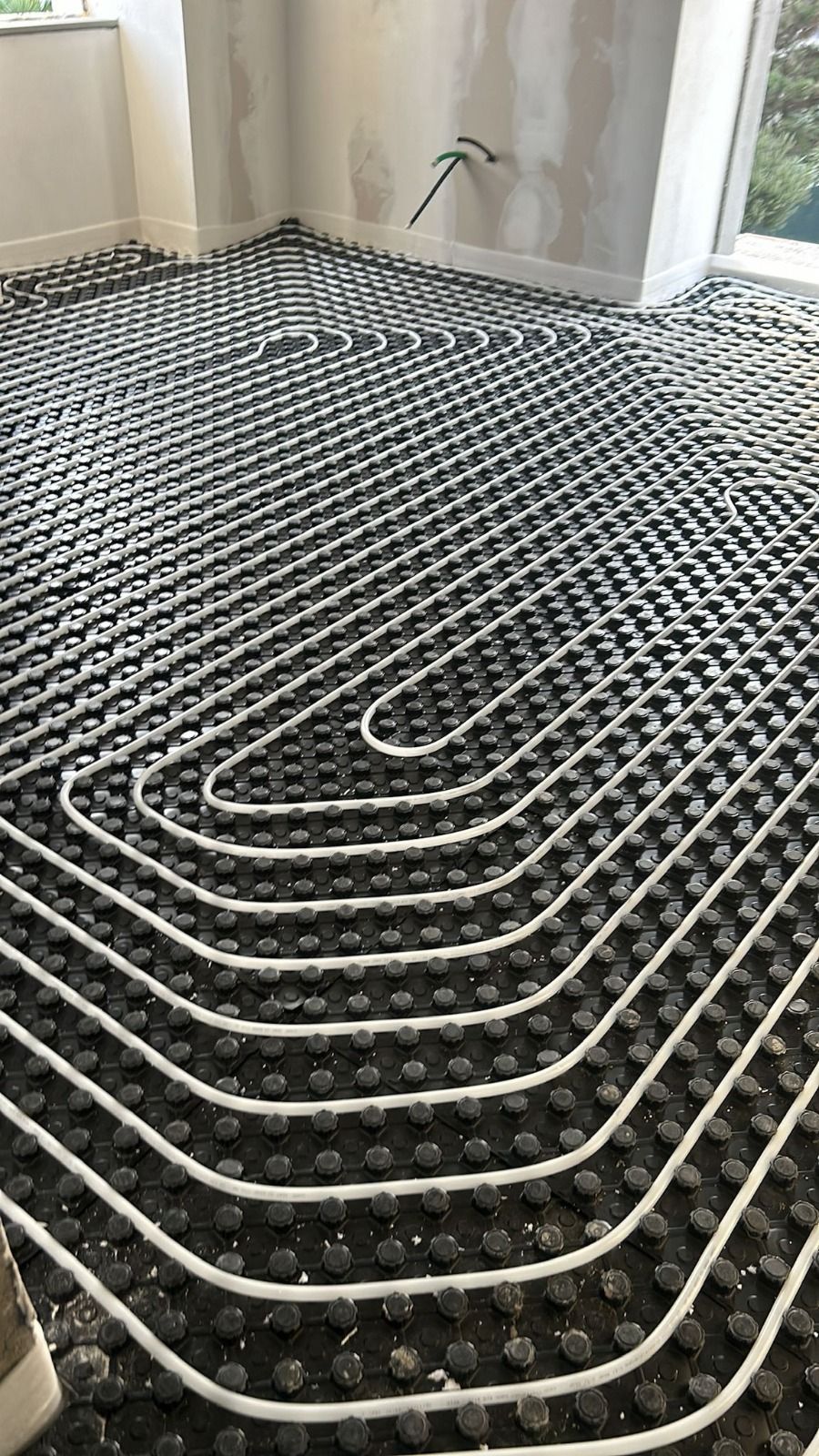 Tubi bianchi disposti a formare uno schema su un isolante nero su un pavimento; una stanza in costruzione.