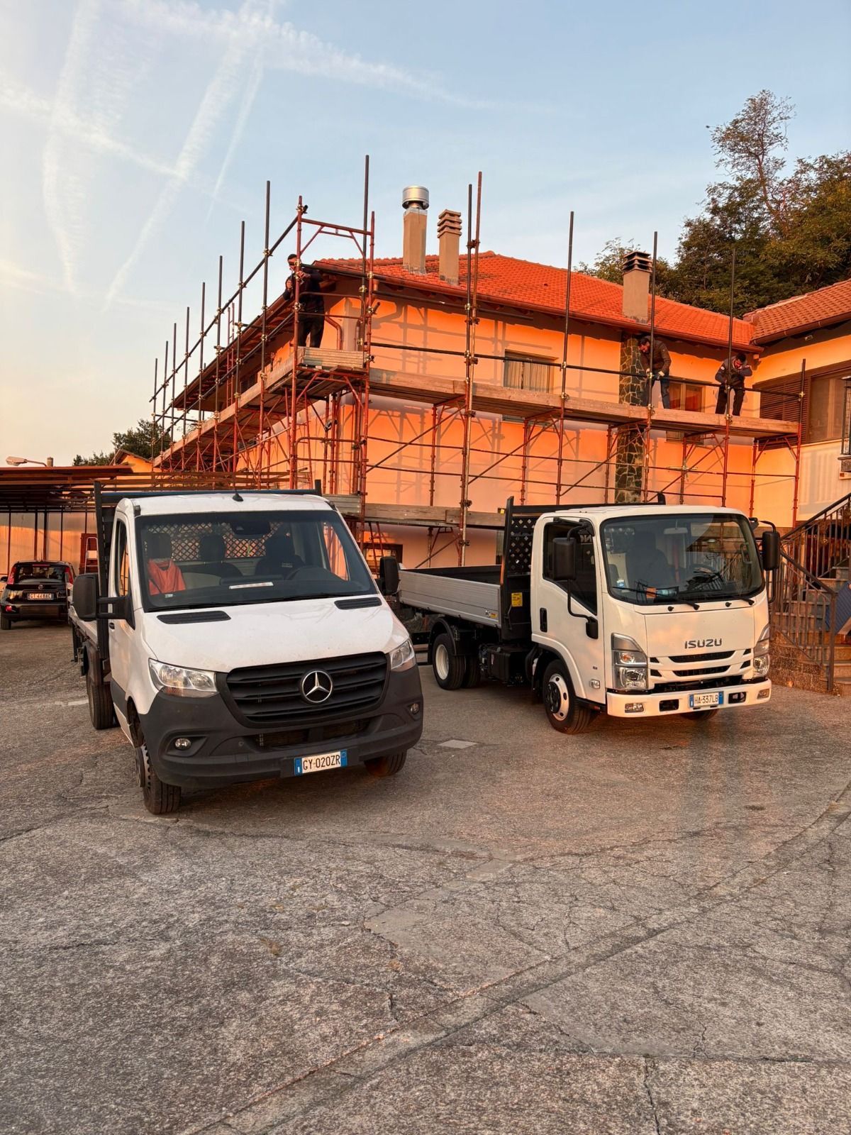 Due camion con pianale parcheggiati vicino a un edificio in costruzione con impalcature.