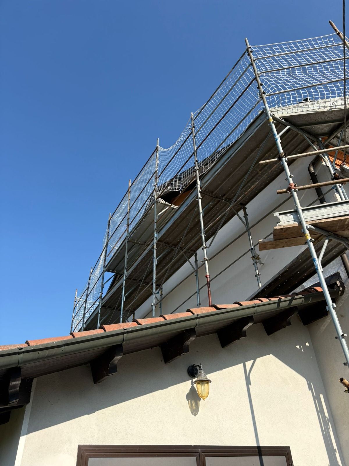 Un'impalcatura appoggiata a un edificio in stucco con un tetto di tegole, sotto un cielo azzurro e terso.
