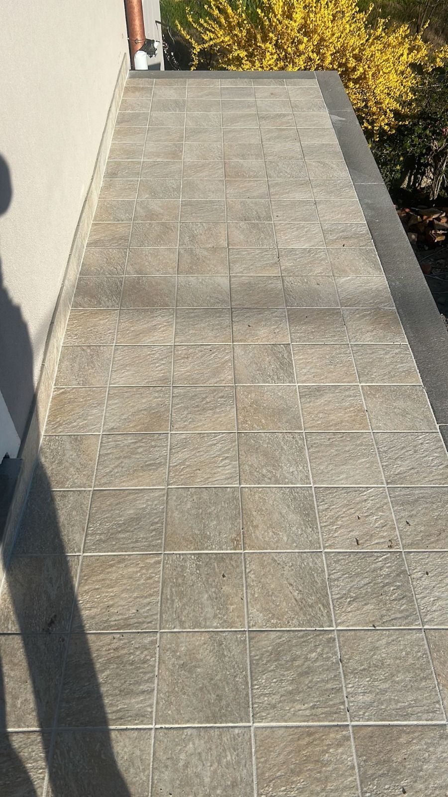 Rampa in pietra che conduce da un edificio a un giardino. Piastrelle grigie, grondaia in bronzo, cespugli gialli.