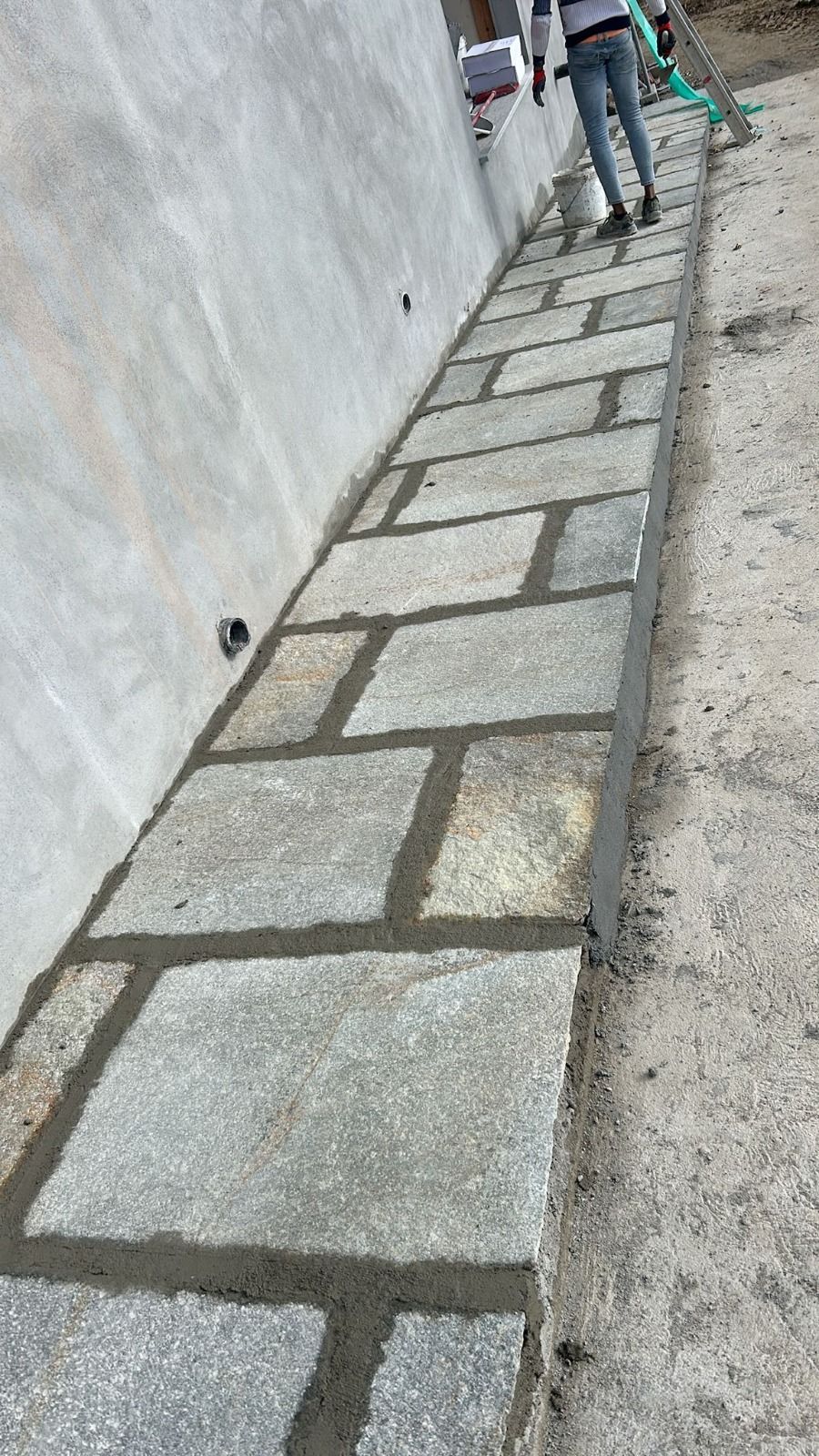 Un sentiero in pietra viene costruito accanto a un muro. Si vede una persona che lavora sul sentiero.