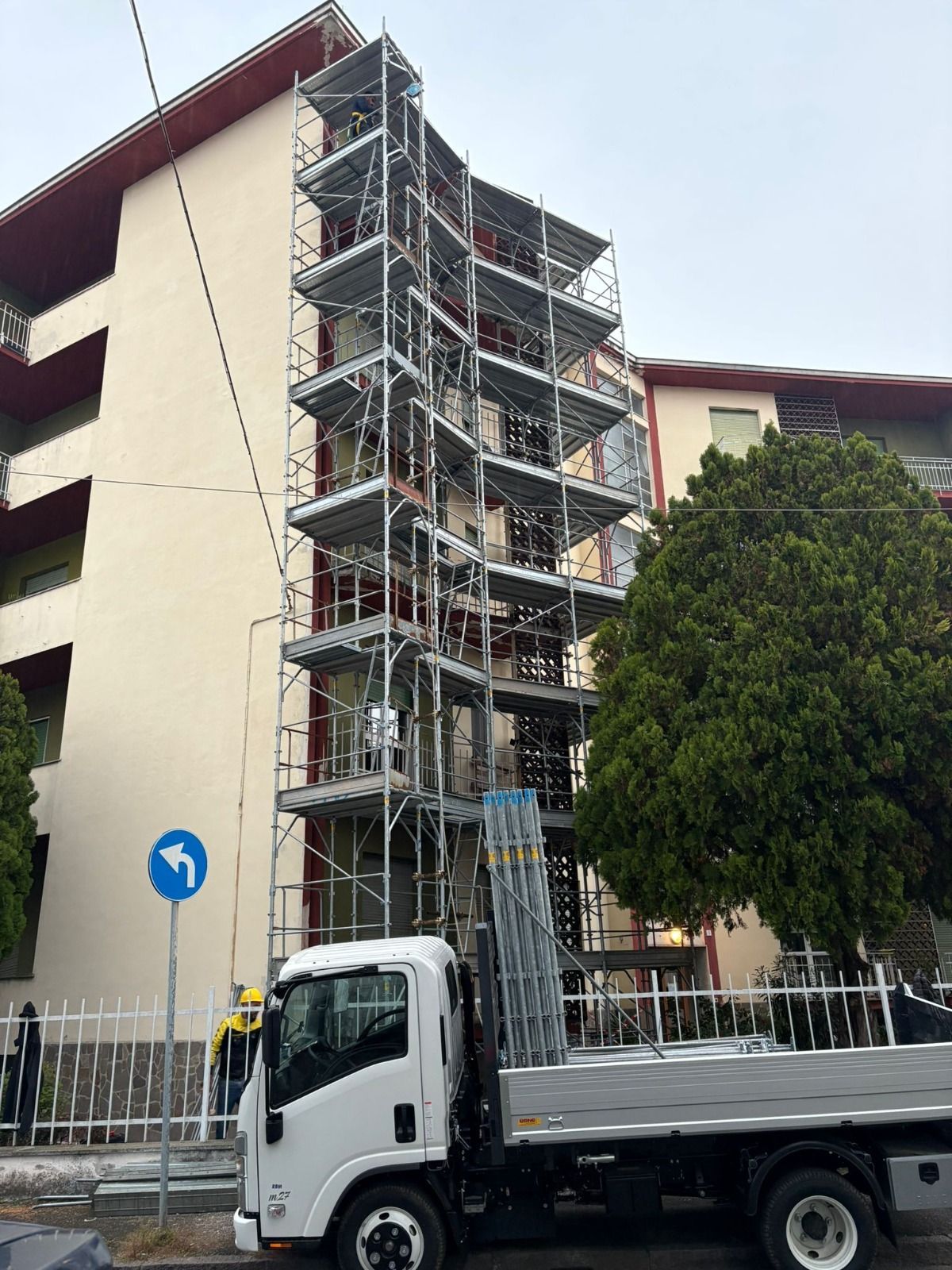 Impalcature all'esterno dell'edificio, camion bianco parcheggiato sotto, cartello stradale.
