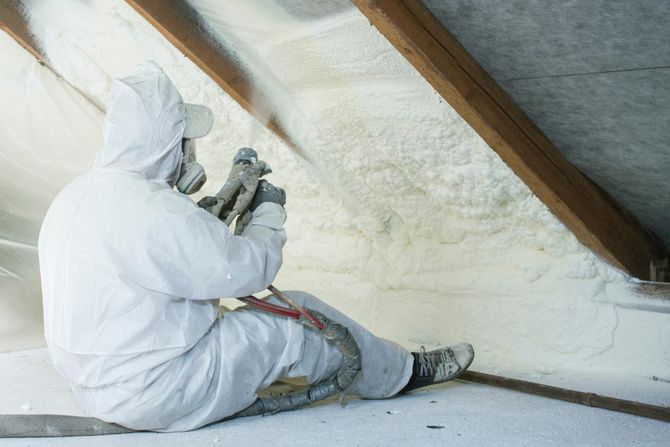 A man in a white suit is spraying insulation on a ceiling.