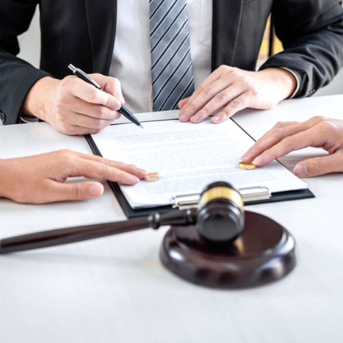 Un juriste et deux personnes examinent un document près d'un maillet en bois, symbolisant un divorce ou un accord légal.