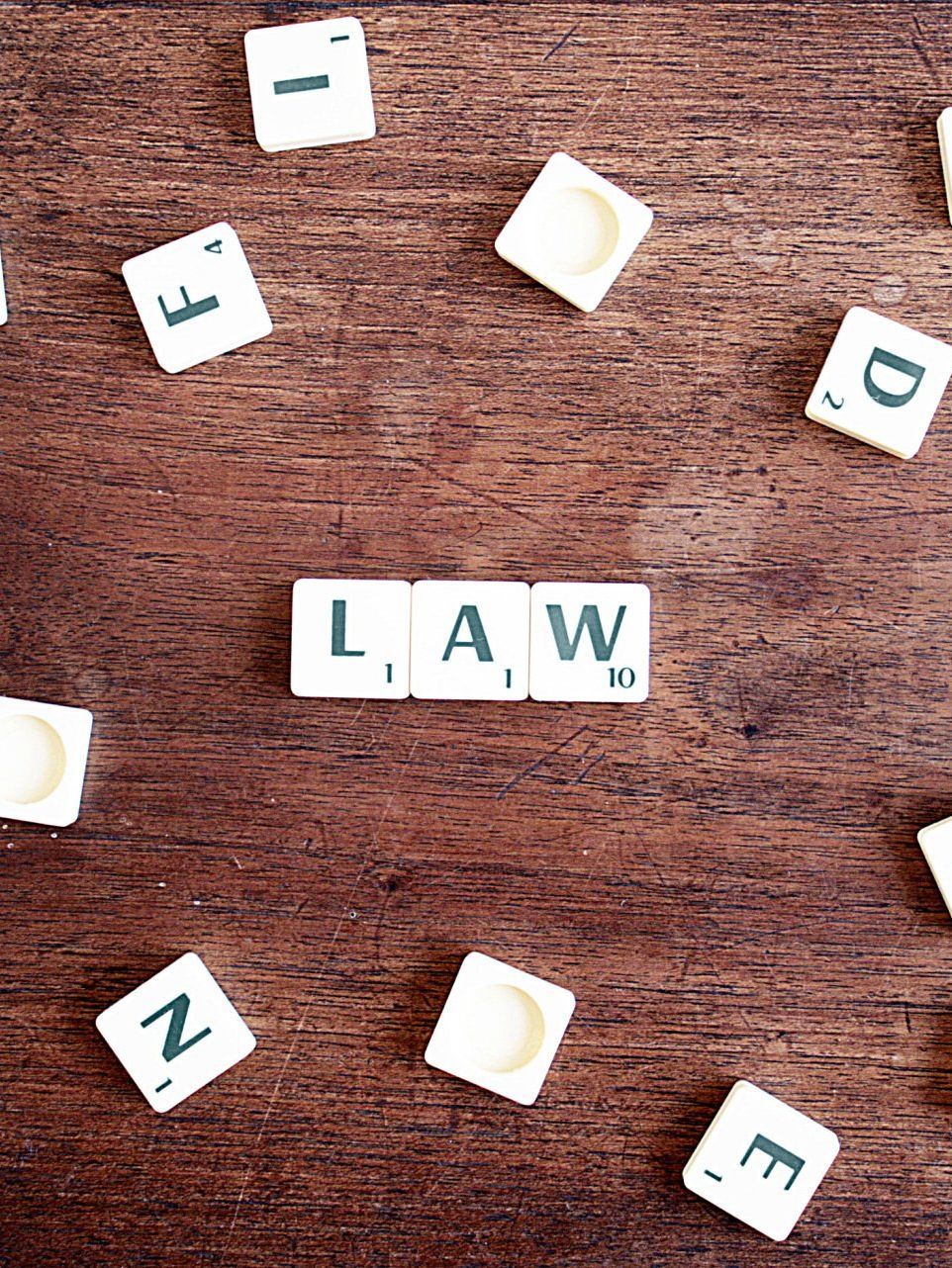 Des lettres de Scrabble sur une surface en bois sombre, avec le mot « LOI » écrit au centre et entouré de lettres éparses.