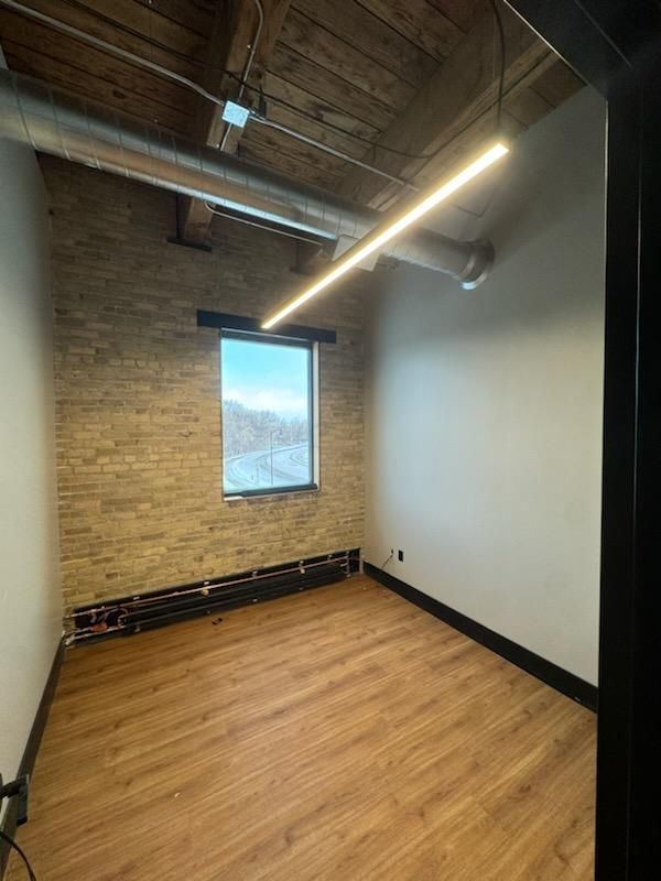 An empty room with hardwood floors , a brick wall and a window.