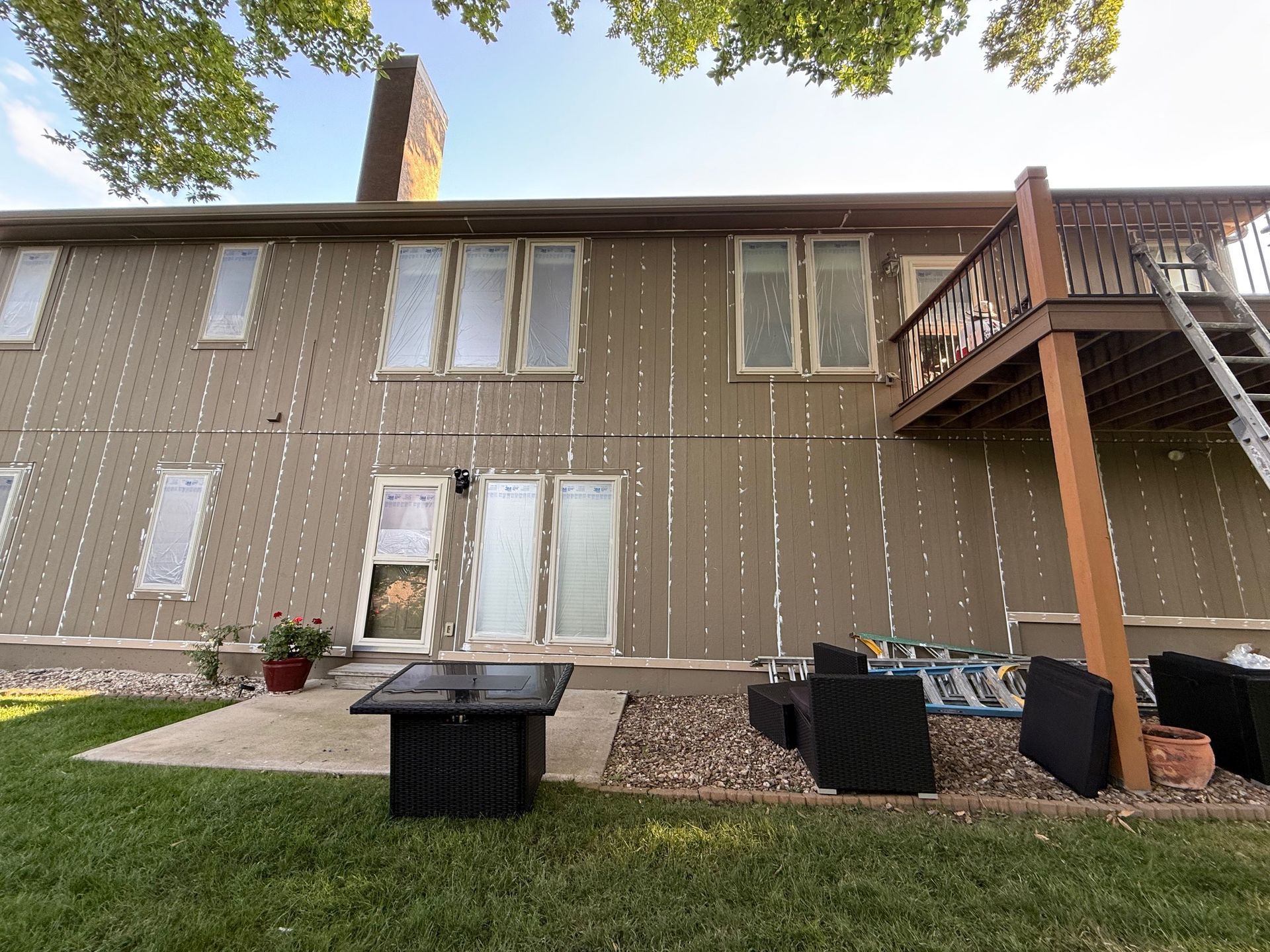 Beige house exterior with sealed windows and a deck, backyard patio with furniture.