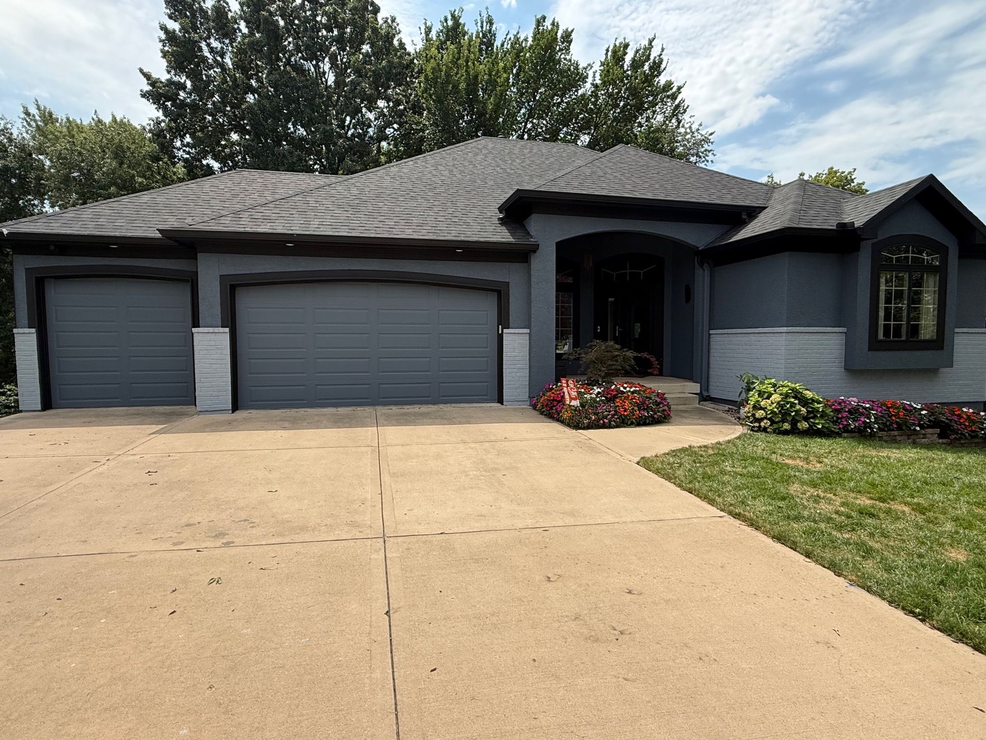 Gray house with a concrete driveway, two-car garage, and colorful flower beds.