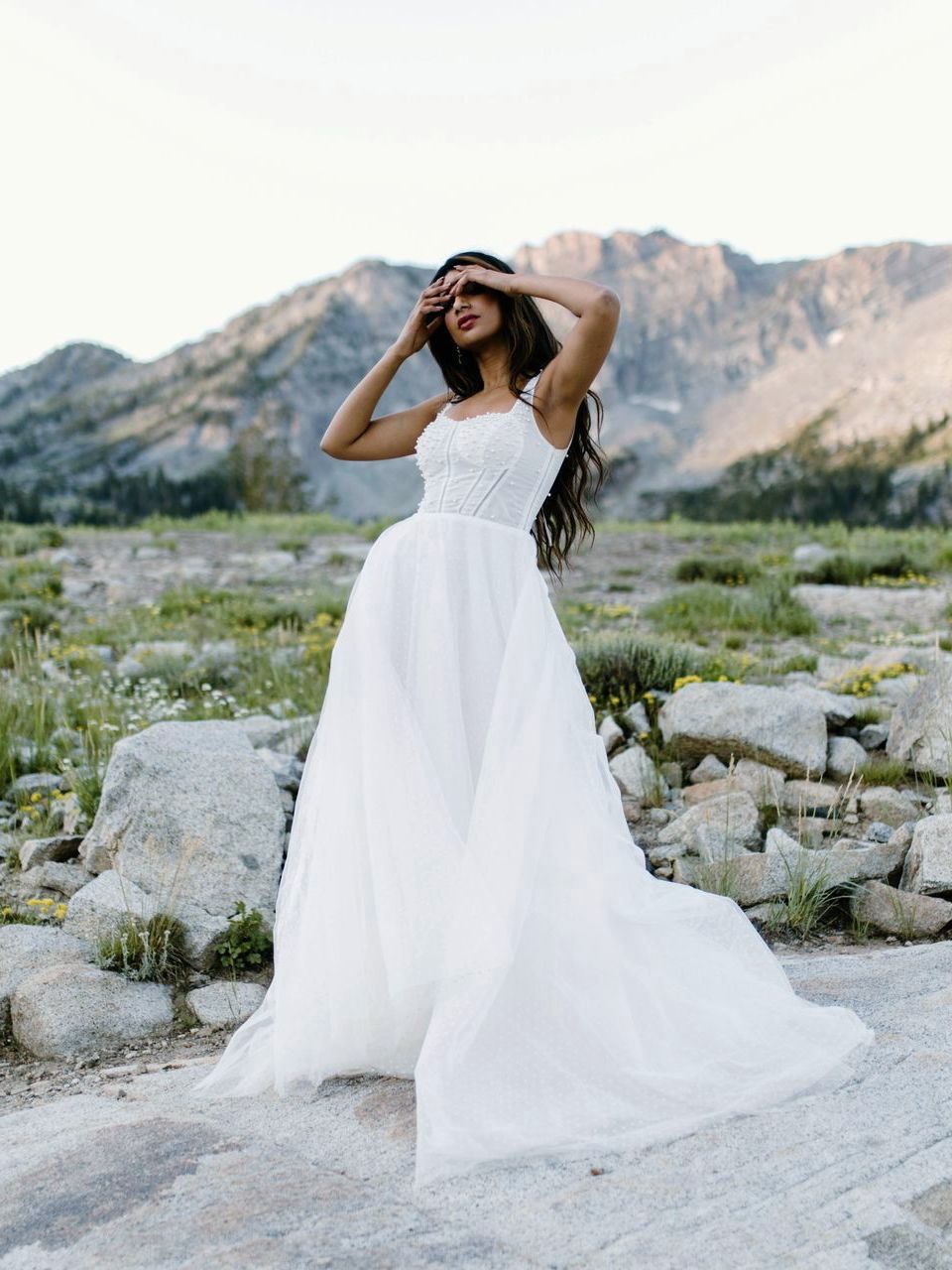 A woman in a white wedding dress is standing in front of a mountain.