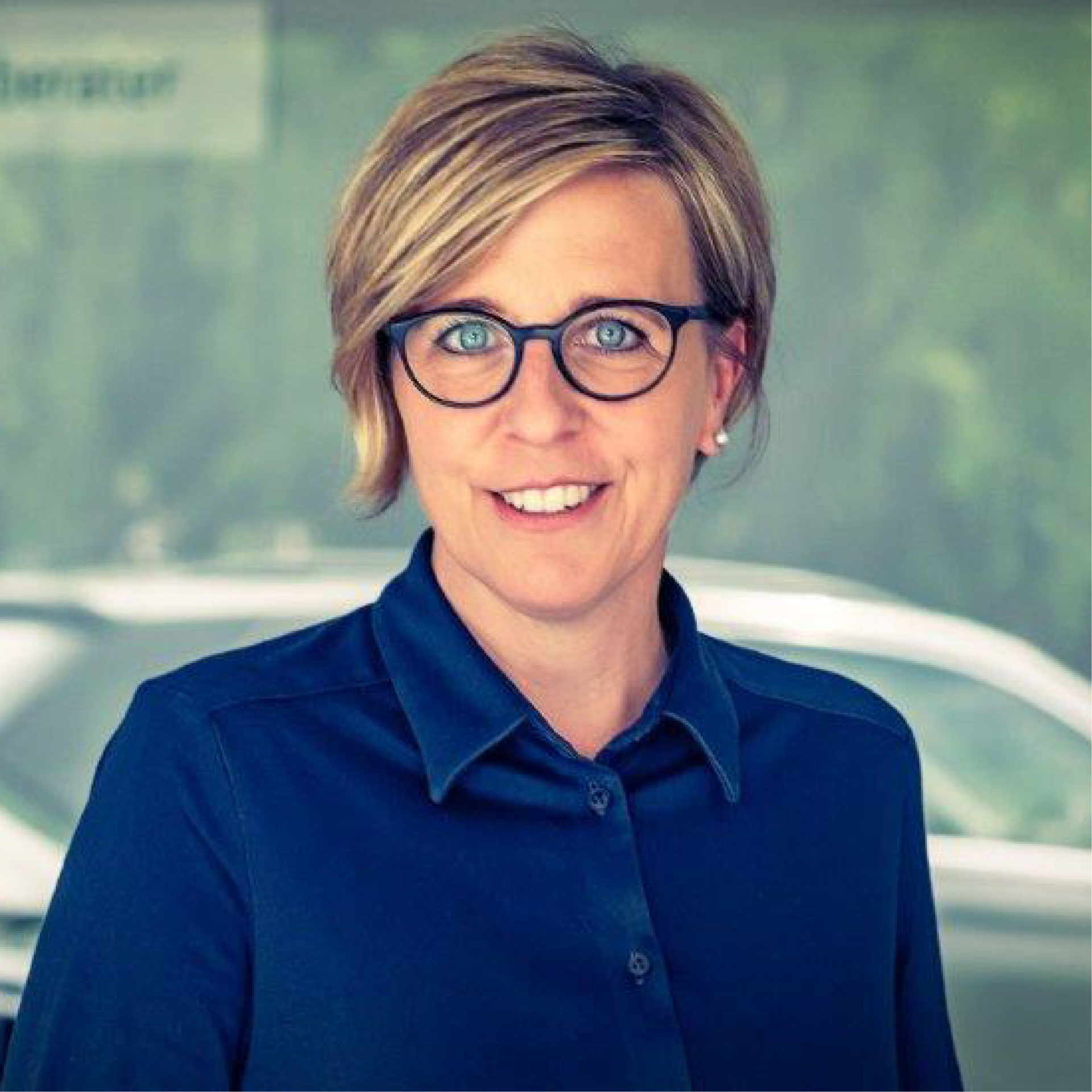 Eine Frau mit Brille und blauem Hemd lächelt in die Kamera