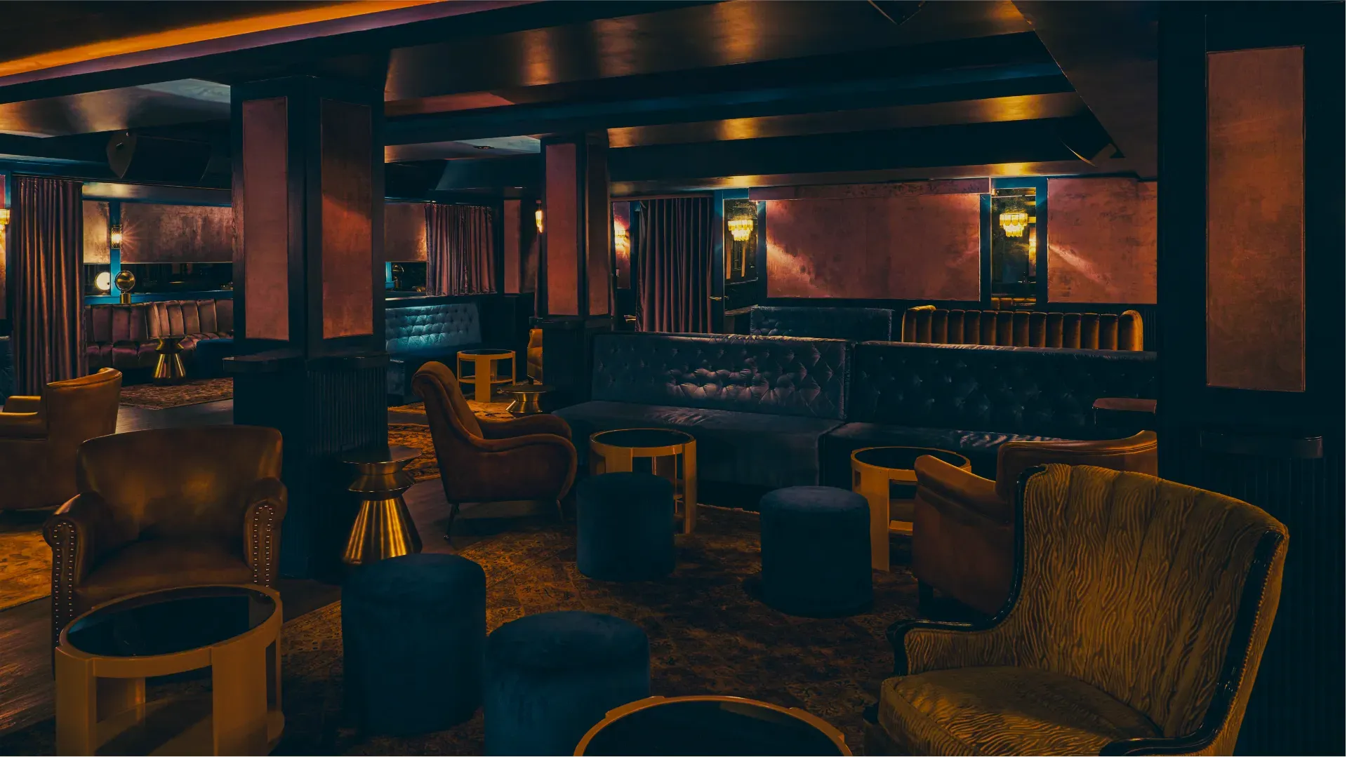 Interior of a dimly lit bar with leather seating, dark wood, and gold accents.