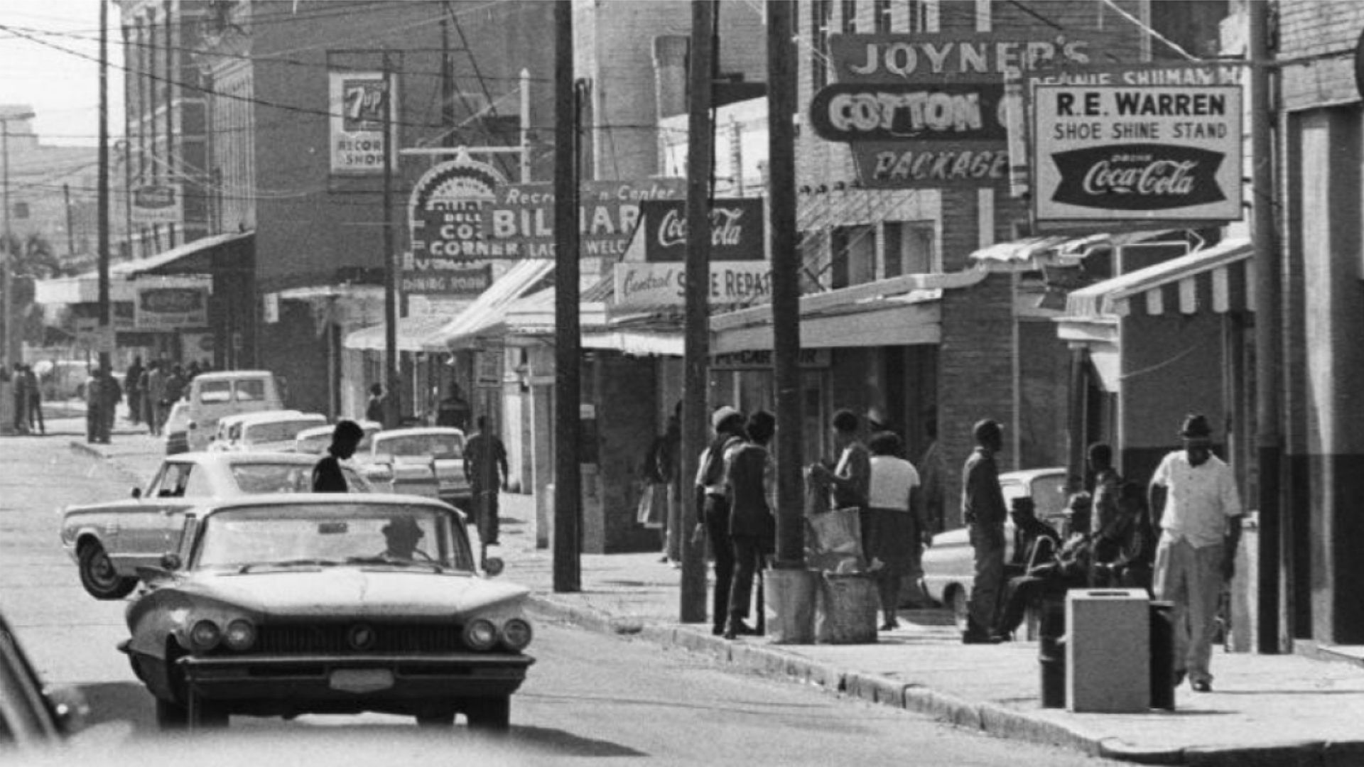 A black and white photo of a city street with a coca cola sign