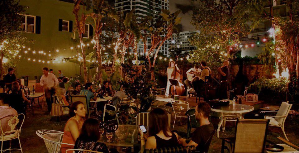 People gathered at an outdoor cafe at night, listening to live music under string lights.
