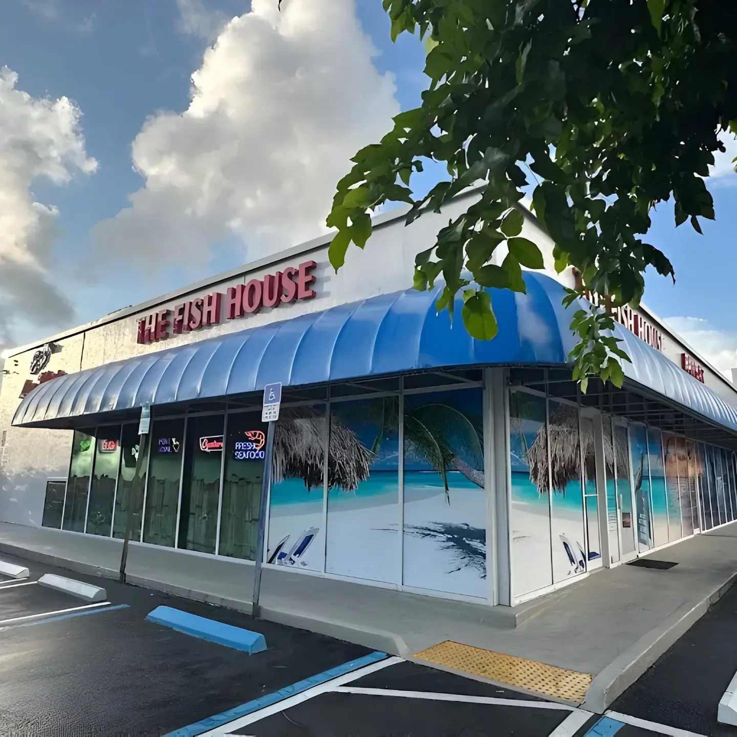 The Fish House restaurant exterior with blue awning and beach scene windows under a blue sky.