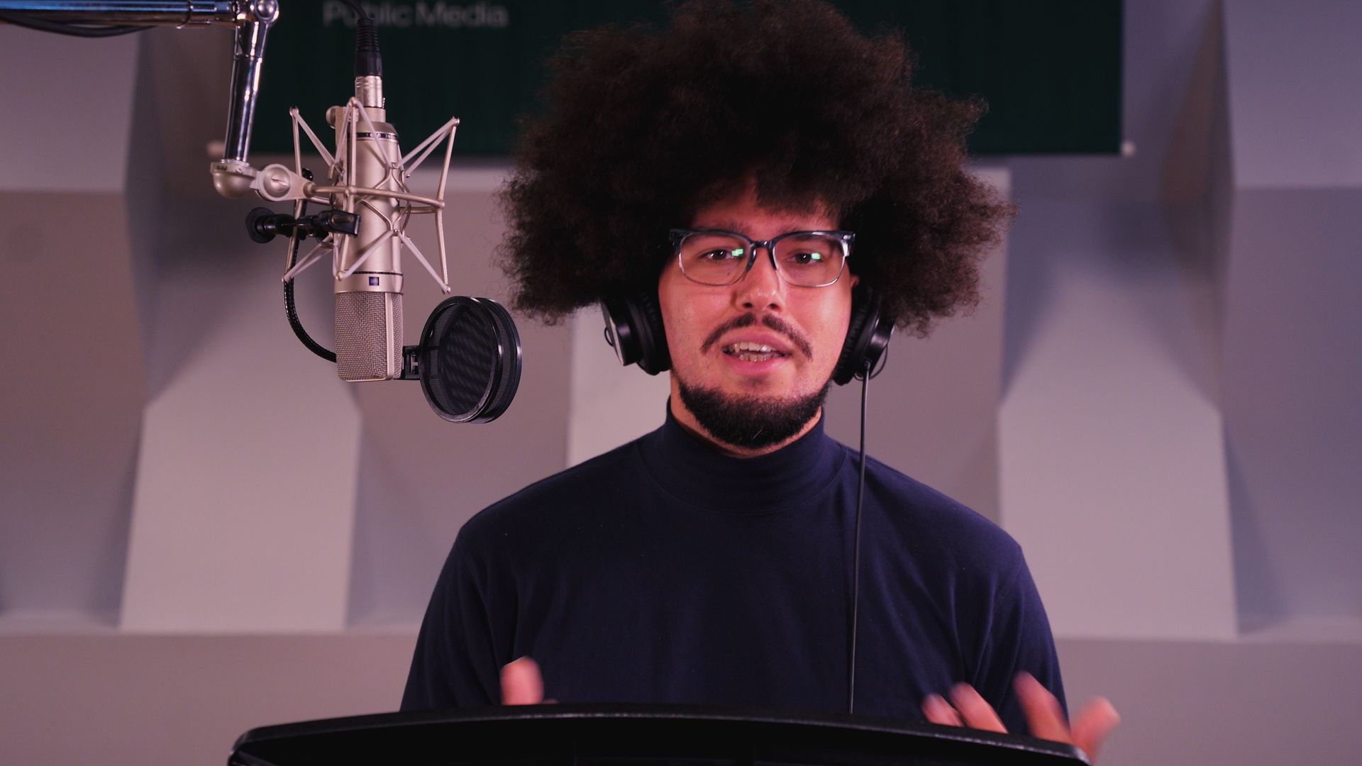 a black man with an afro and glasses is standing in front of a microphone