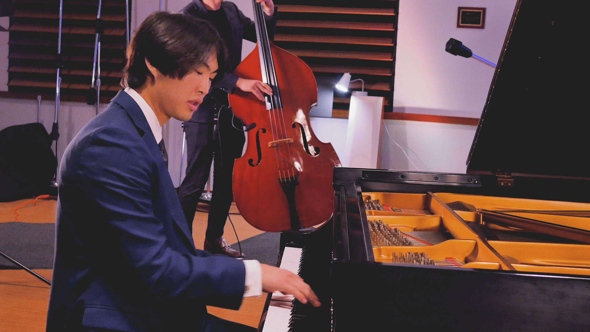 A man in a suit is playing a piano while another man plays a double bass.