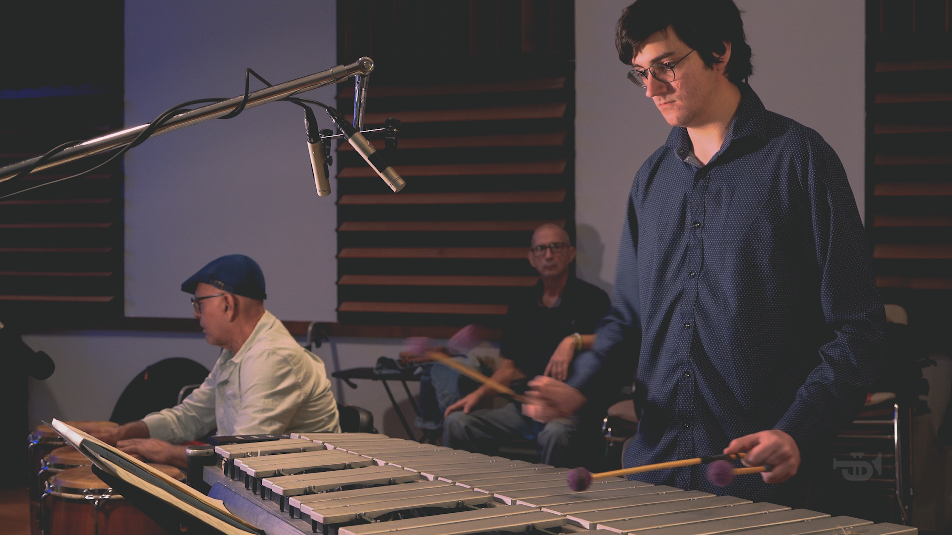 A man is playing a marimba in front of a microphone in a recording studio.