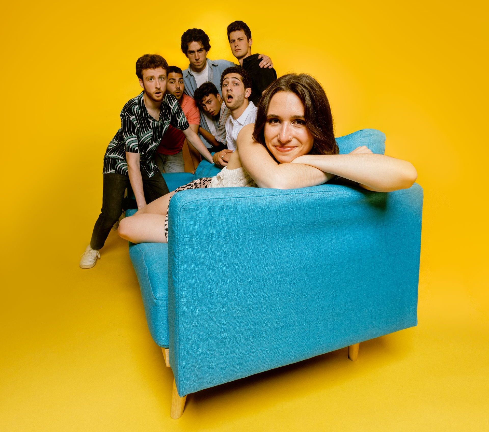a group of people are posing for a picture with a woman laying on a blue couch