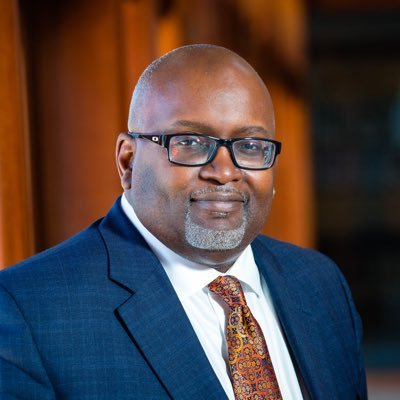 A man in a suit and tie is wearing glasses and a beard.