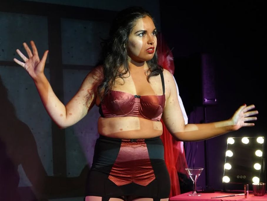 A woman in lingerie is standing on a stage with her arms outstretched