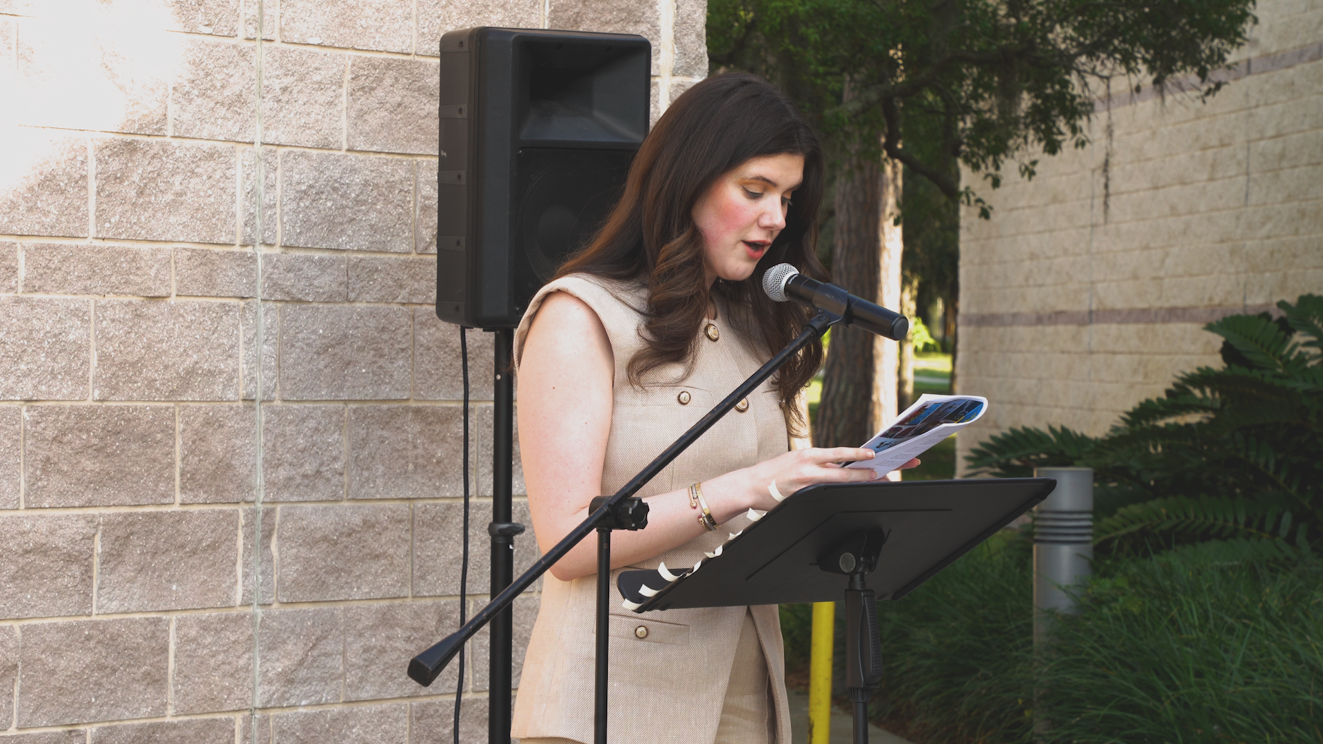 A woman is standing in front of a microphone reading a book.