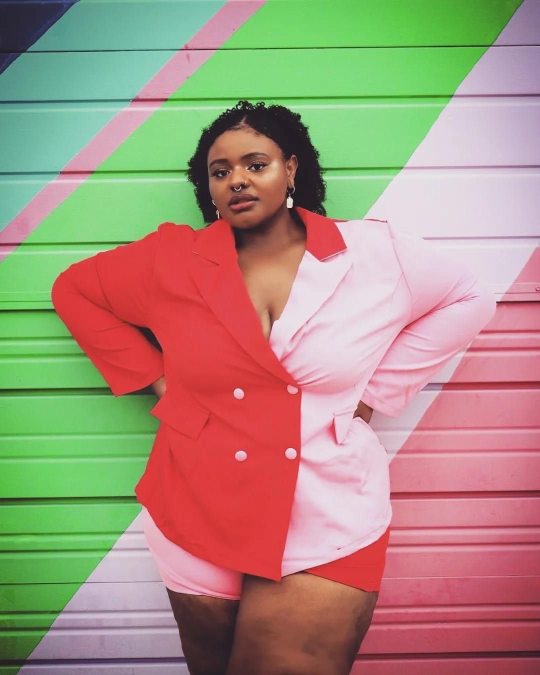 a woman in a red and pink suit stands in front of a colorful wall