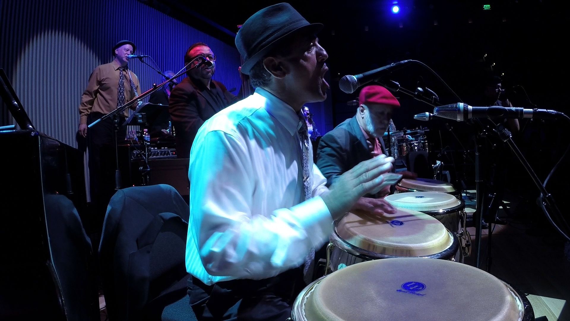 A man in a hat is playing drums in a band on a stage.