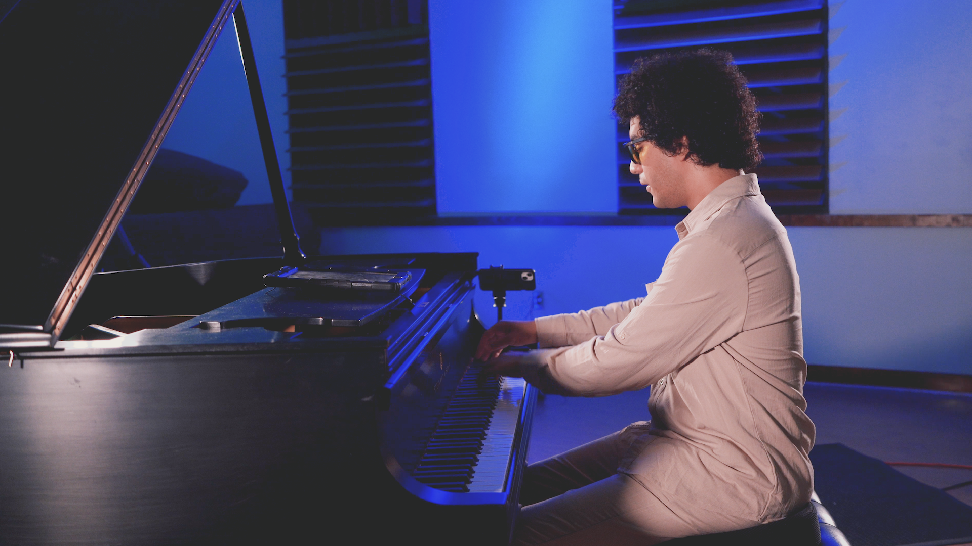 A man is sitting on a stool playing a piano in a room.