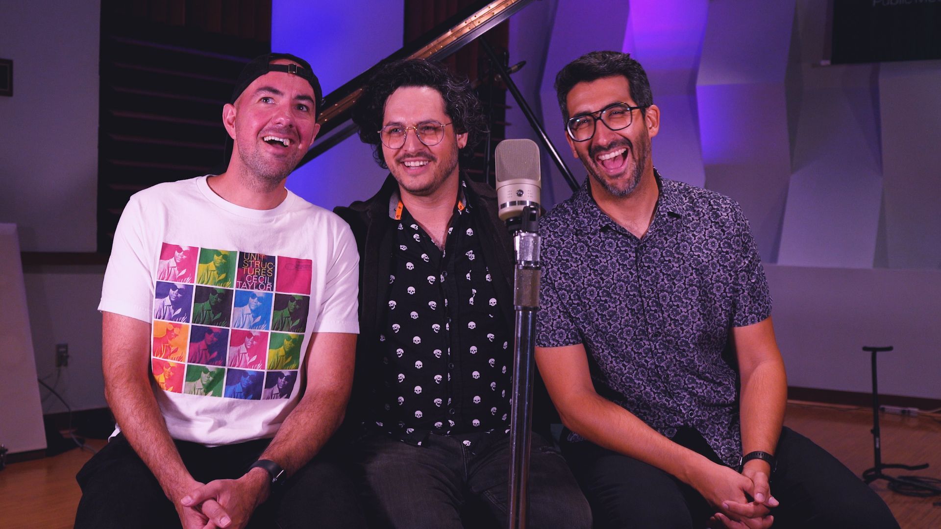 Three men are sitting next to each other in front of a microphone in a room.