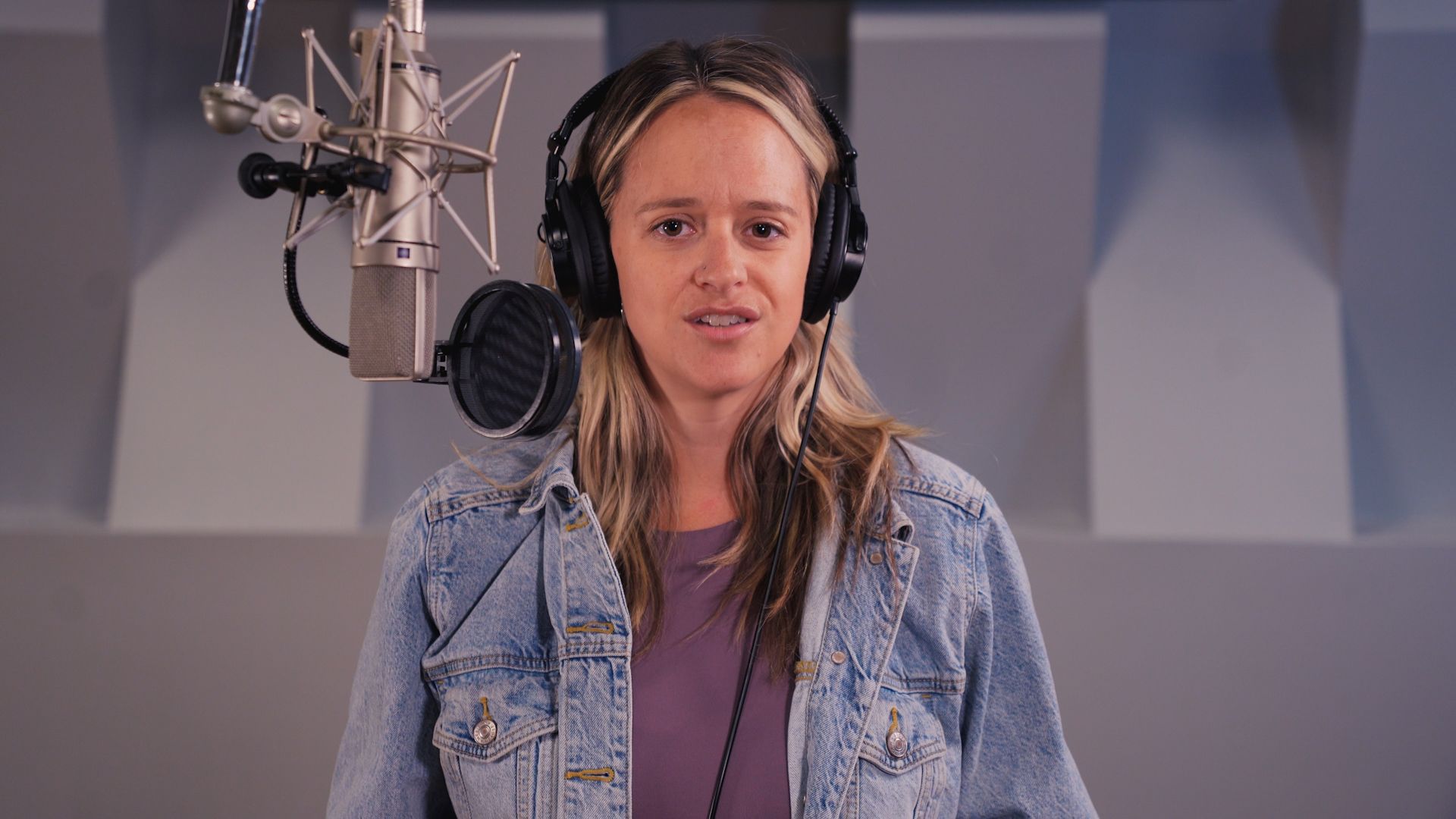 a woman wearing headphones is singing into a microphone in a recording studio .