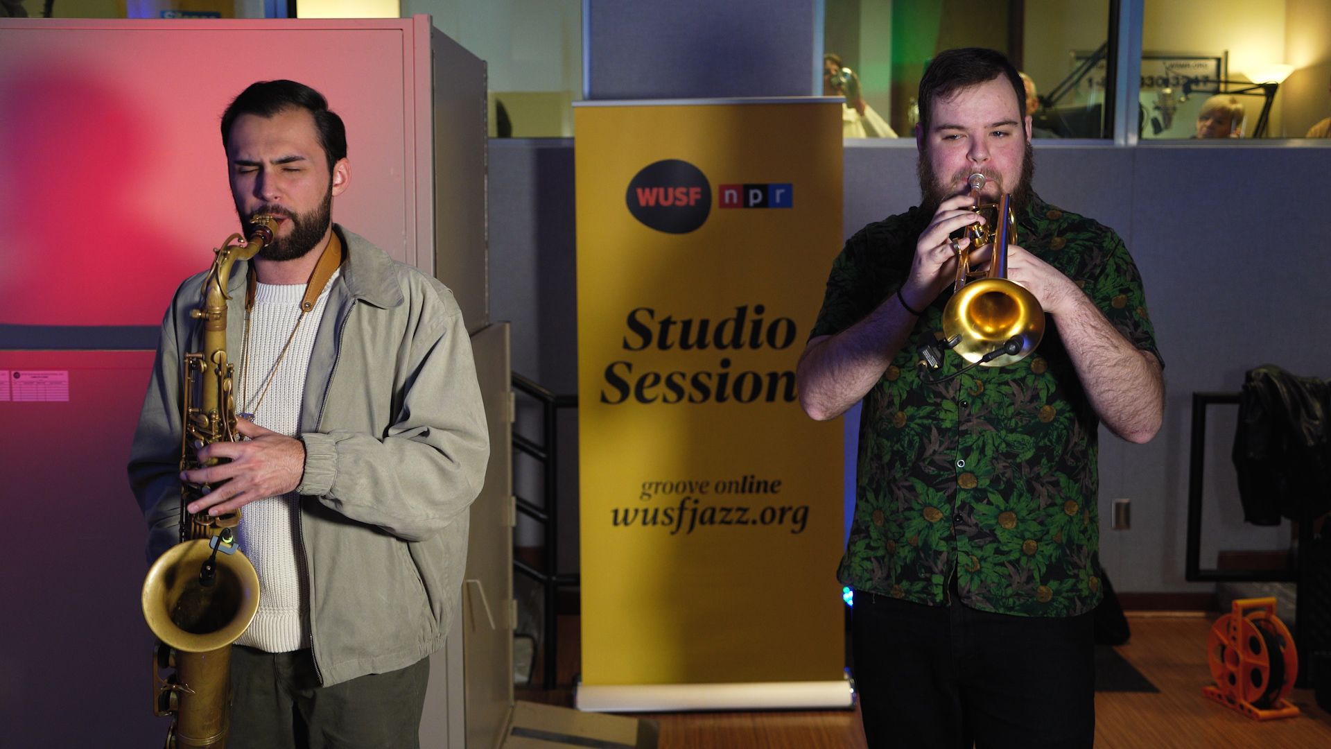 Two saxophonists performing on stage beside a “Studio Session” banner.