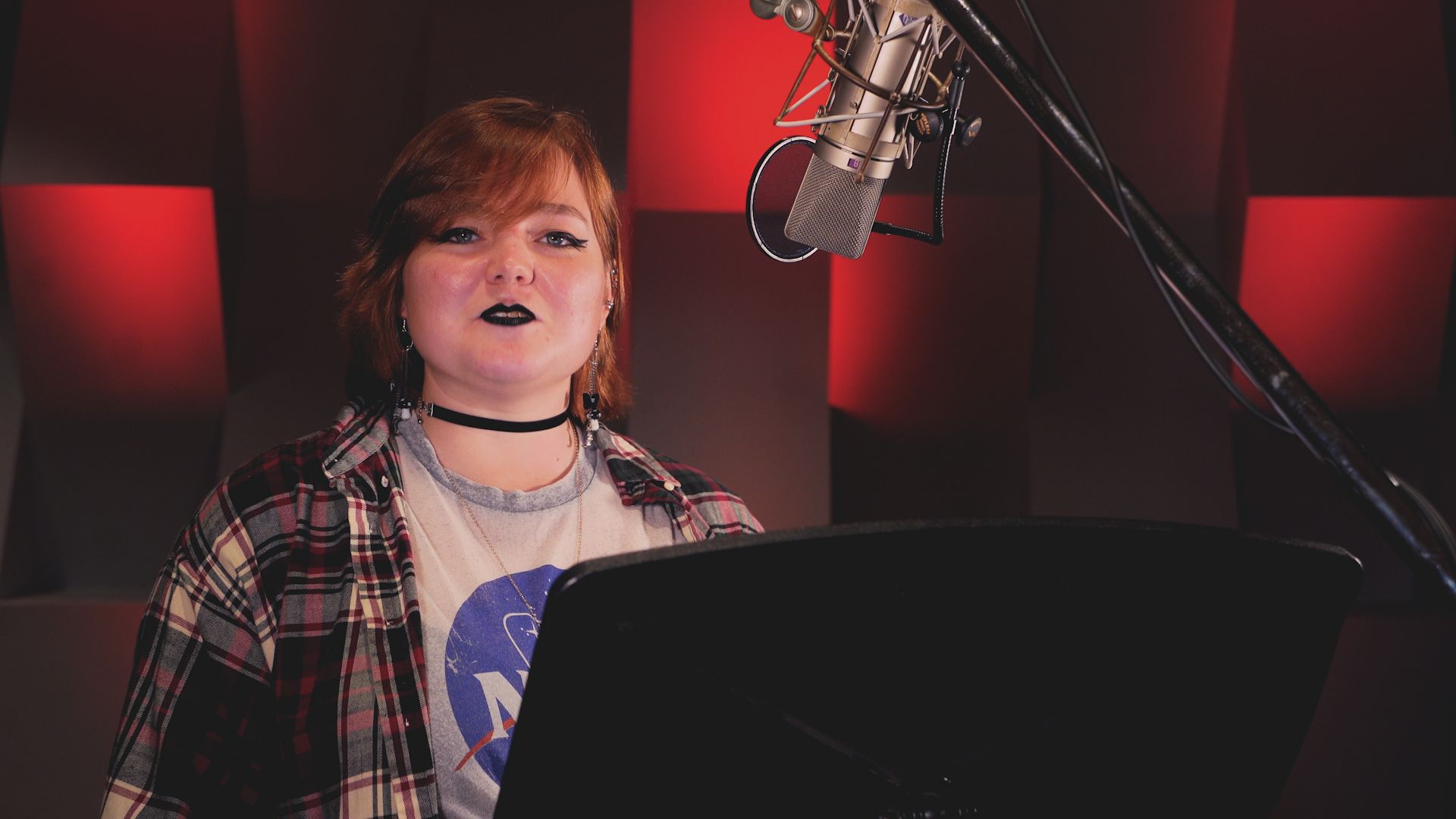 A woman is singing into a microphone in a recording studio.