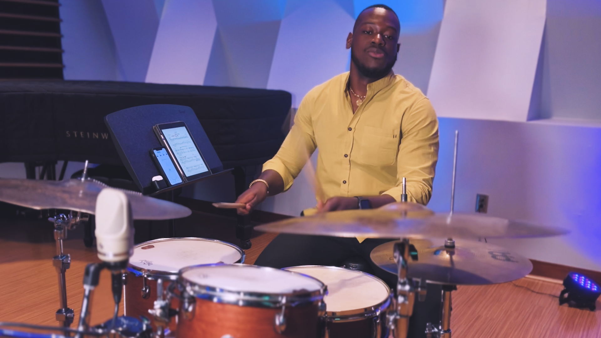 A man in a yellow shirt is playing drums in a room.