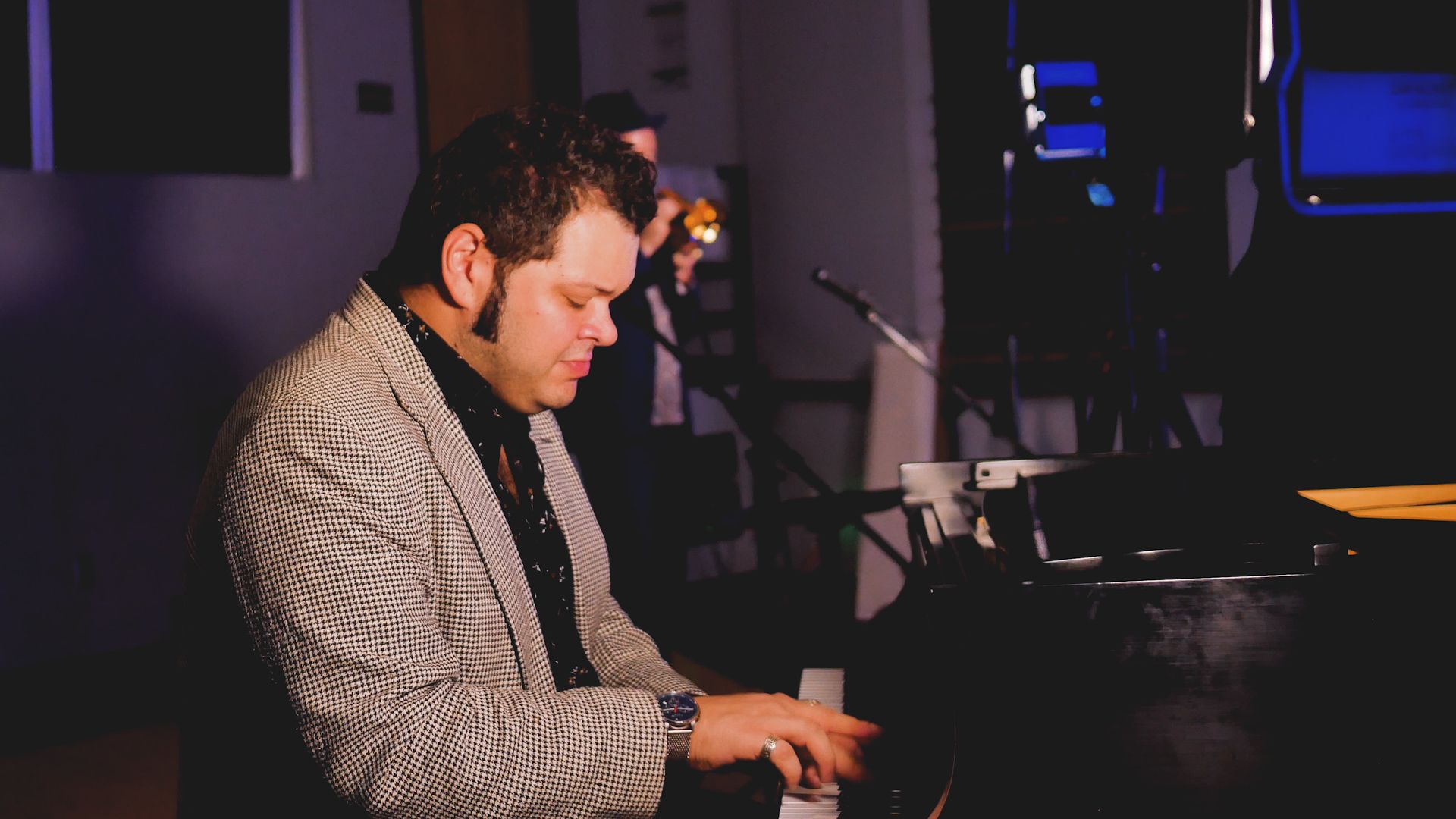 A man in a suit is playing a piano in a dark room.