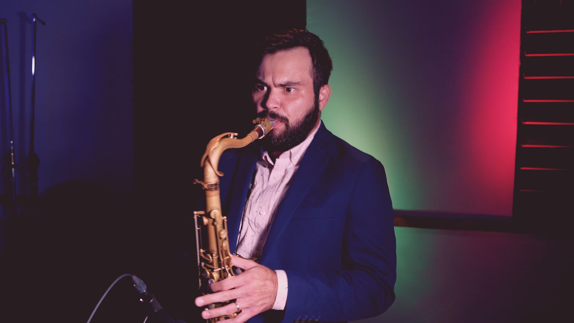 A man with a beard is playing a saxophone in a dark room.