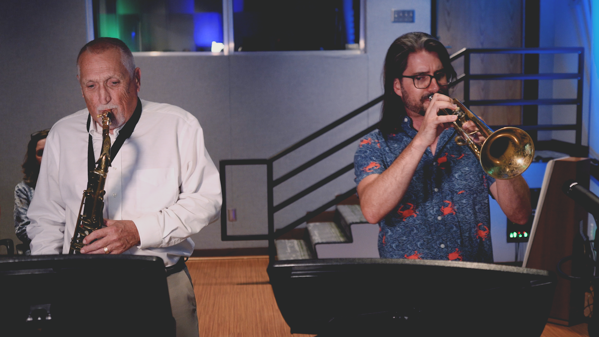 Two men are playing saxophones and trumpets in a room.