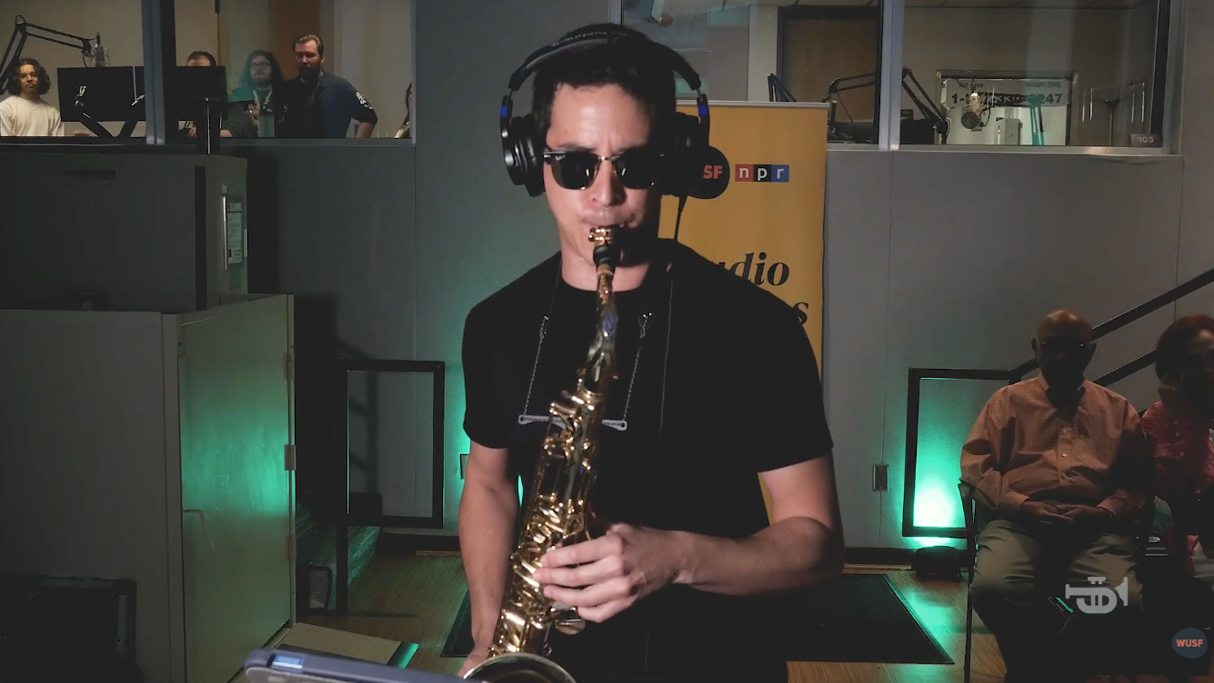 Man in sunglasses plays a saxophone in a radio studio.