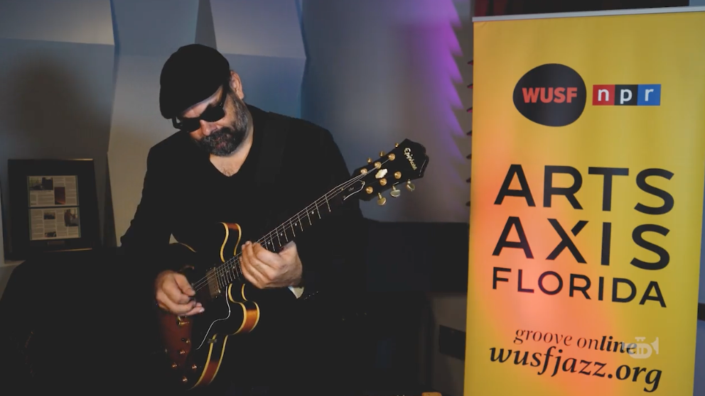 Musician in black cap playing guitar beside WUSF NPR Arts Axis Florida event banner