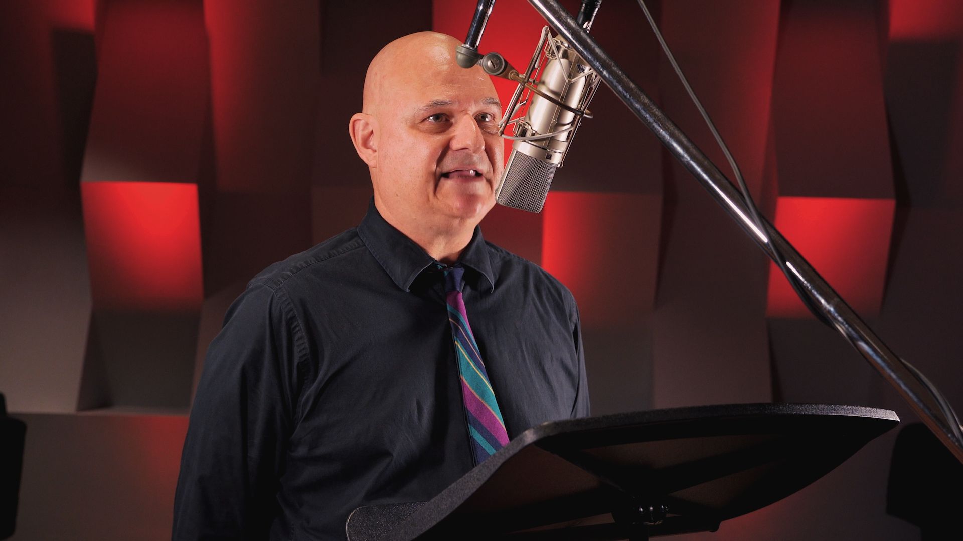 a man in a black shirt and tie is singing into a microphone .
