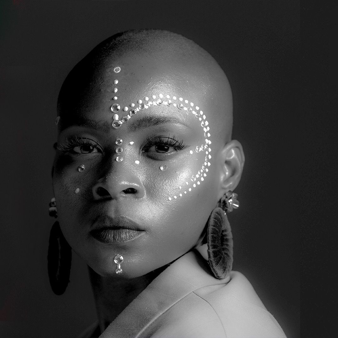A black and white photo of a woman with a shaved head and earrings.