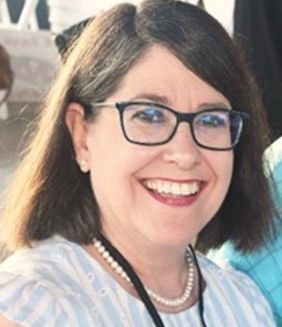 A woman wearing glasses and a pearl necklace is smiling for the camera.