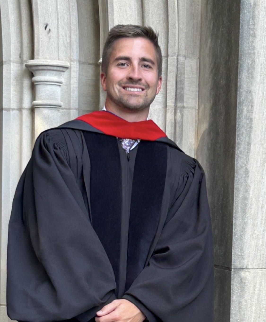 A man in a graduation cap and gown is smiling