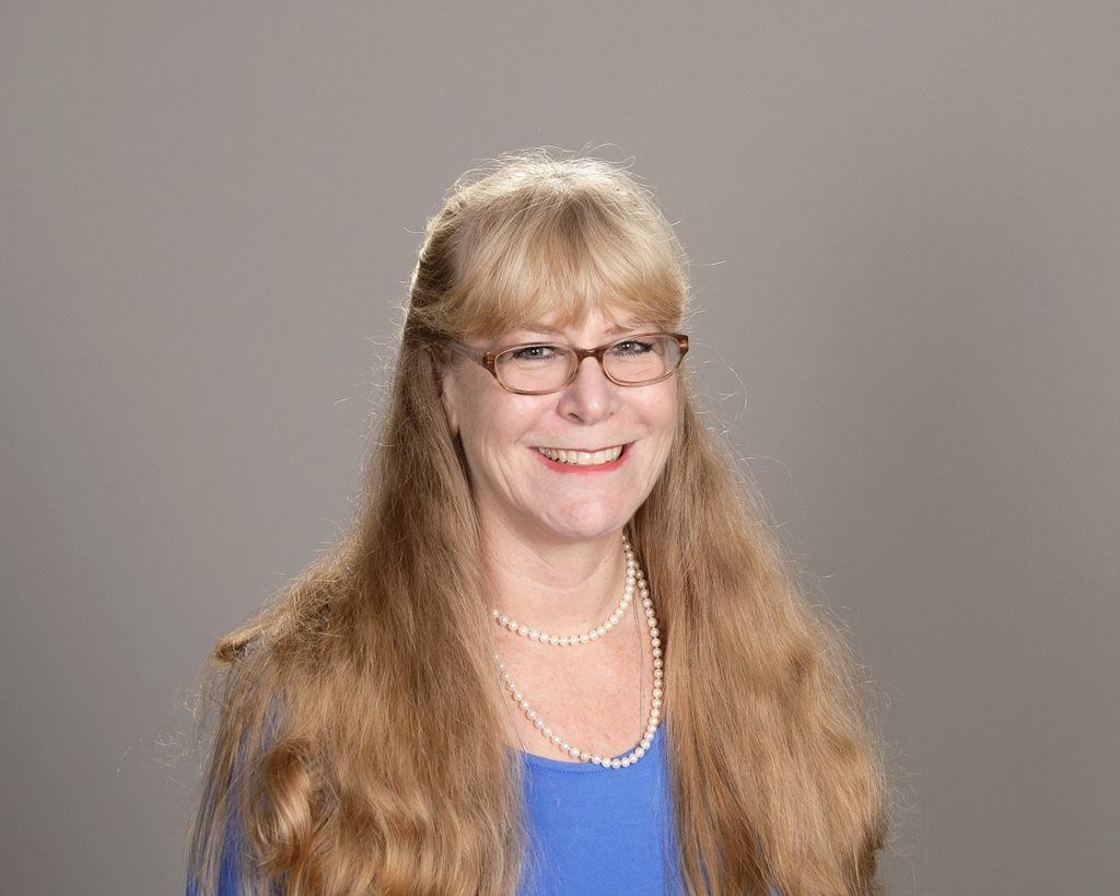 A woman wearing glasses and a pearl necklace is smiling for the camera.